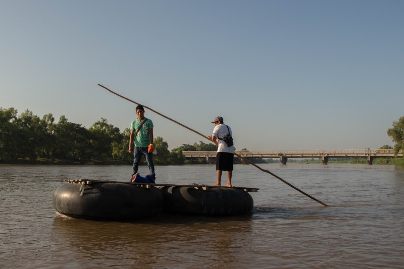 Two men cross the Suchiate River, which borders Guatemala and Mexico. In the background, we can see a bridge that houses a migratory checkpoint. Photo by Gabriela Bortolamedi.